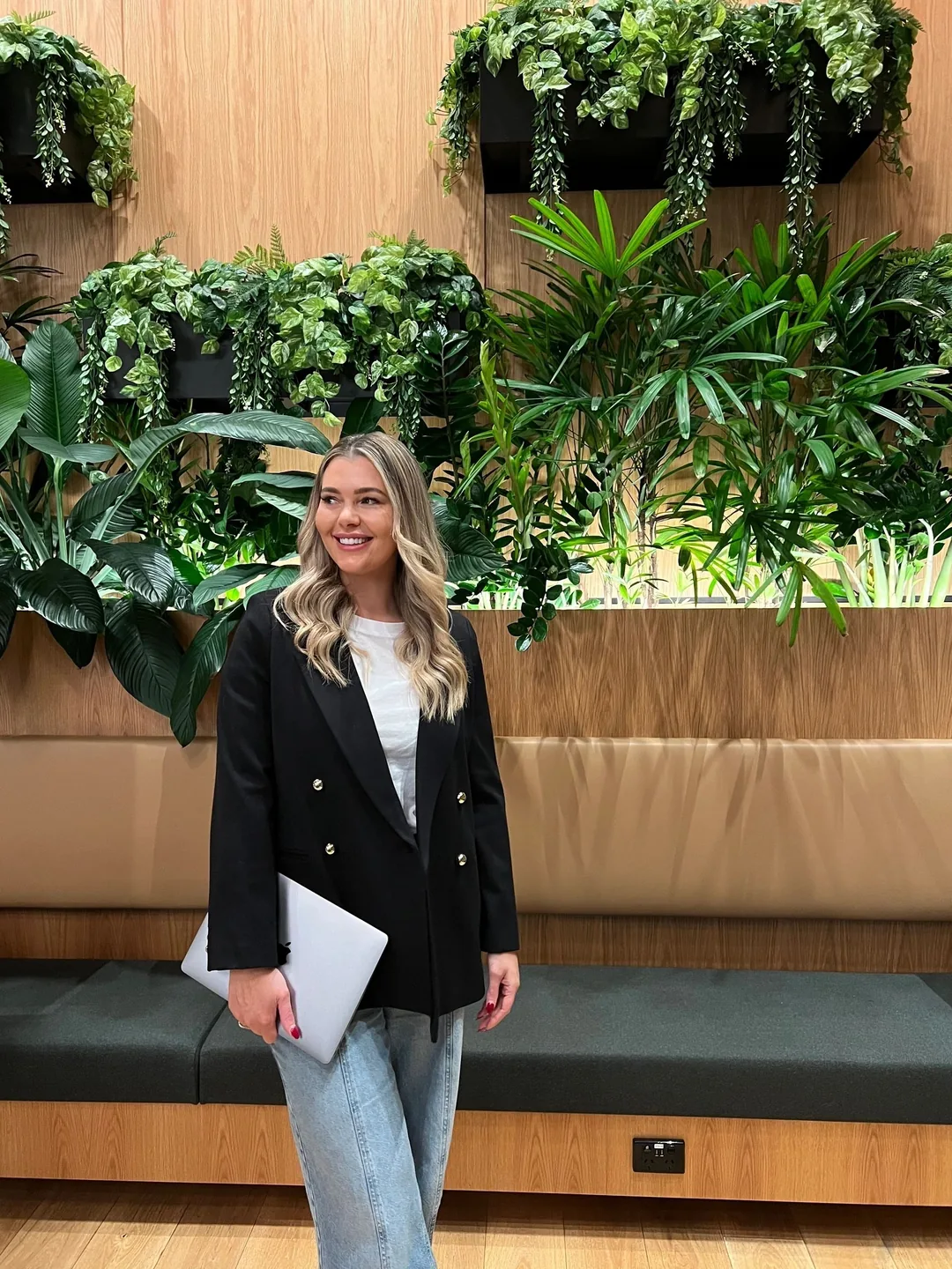 Krystle standing with a laptop in front of an indoor garden