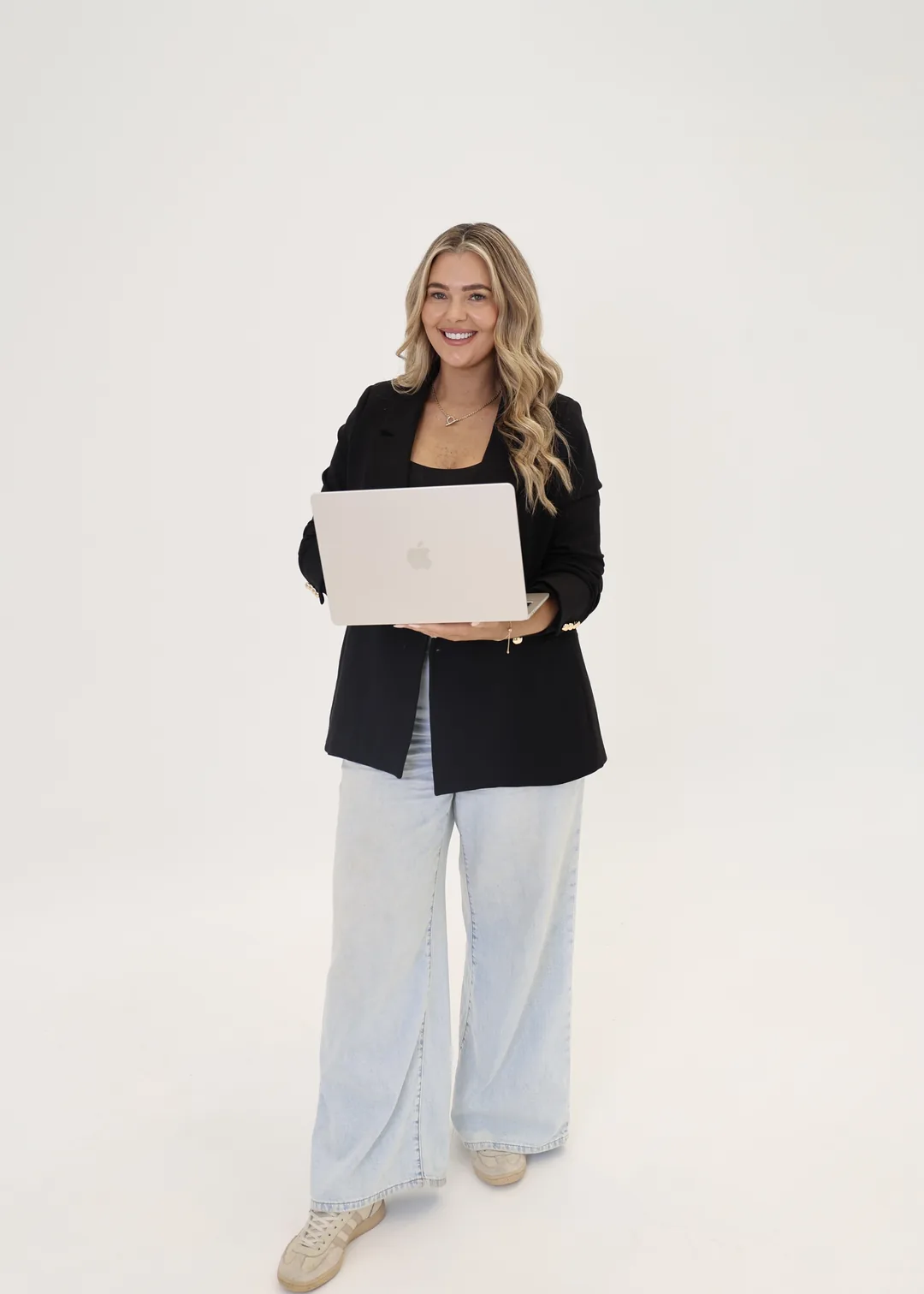 Krystle smiling behind an open laptop in a black blazer