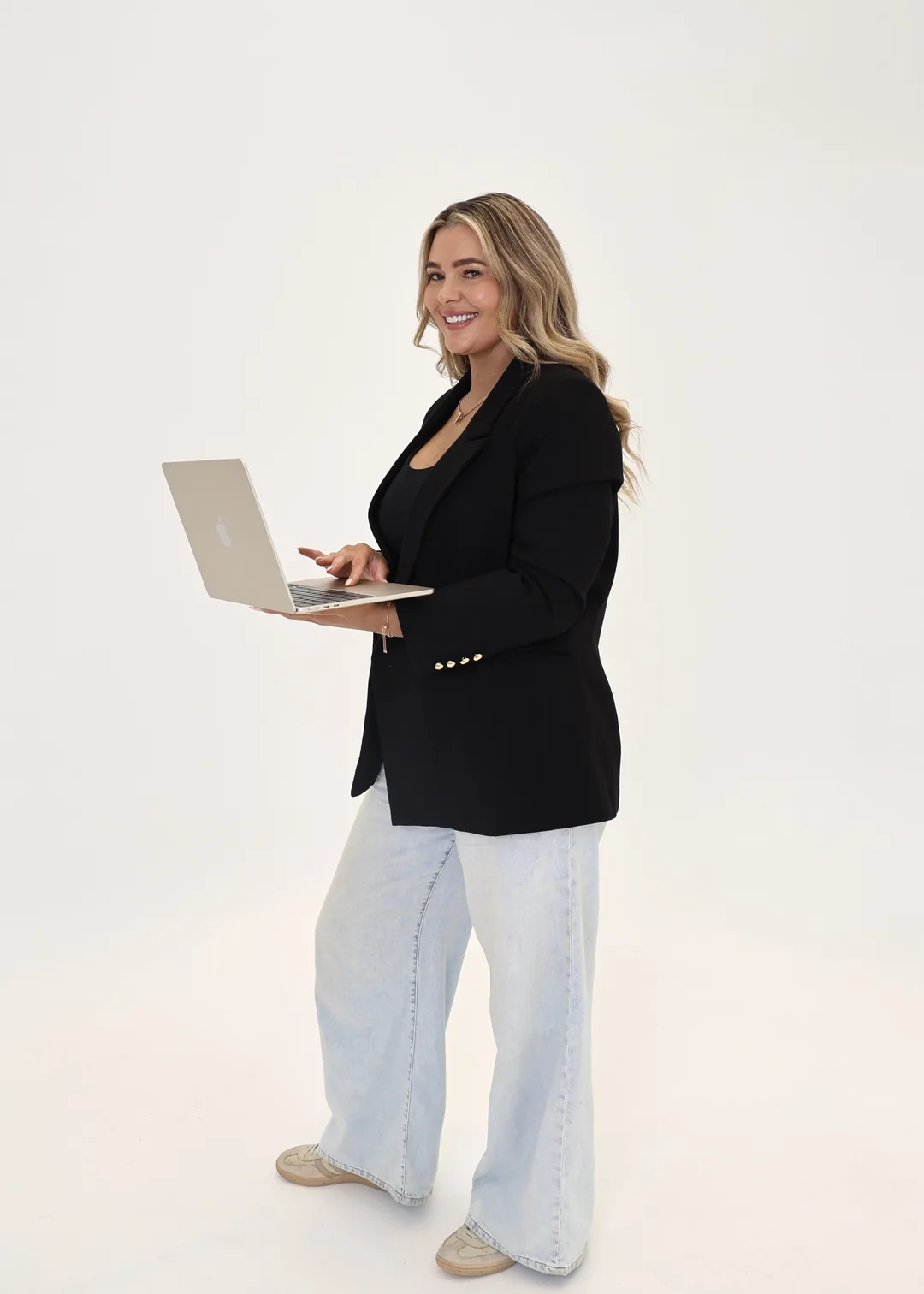 Krystle standing with an open laptop in a black blazer