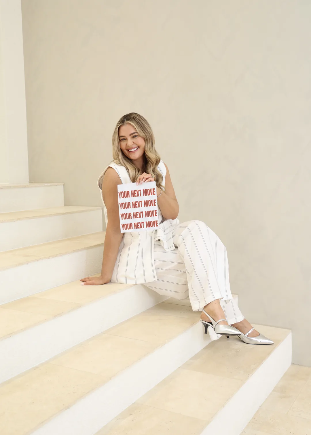 Krystle seated on cream steps, holding a sign that reads Your next move