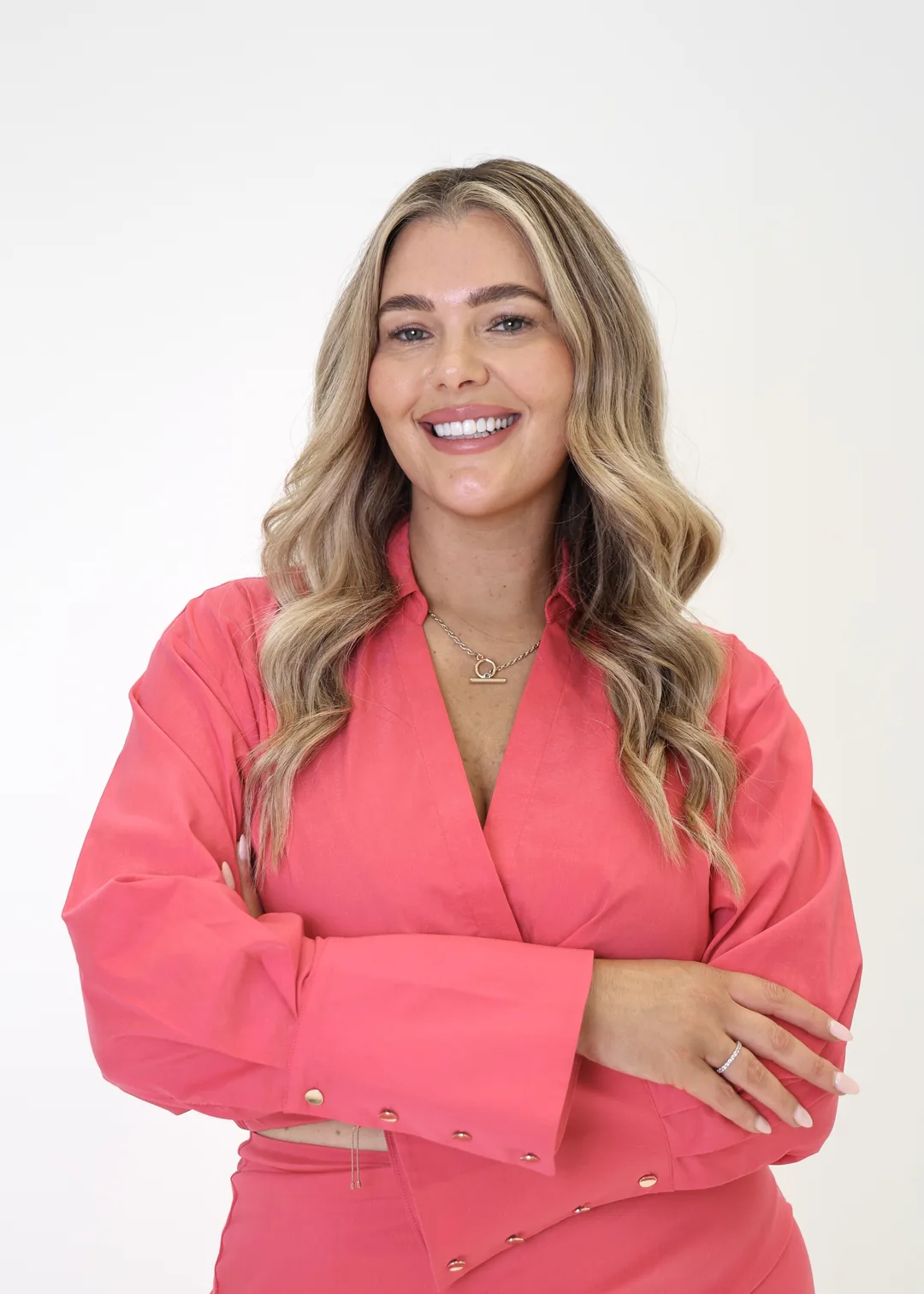 Krystle smiling in a bright pink suit against a cream studio backdrop