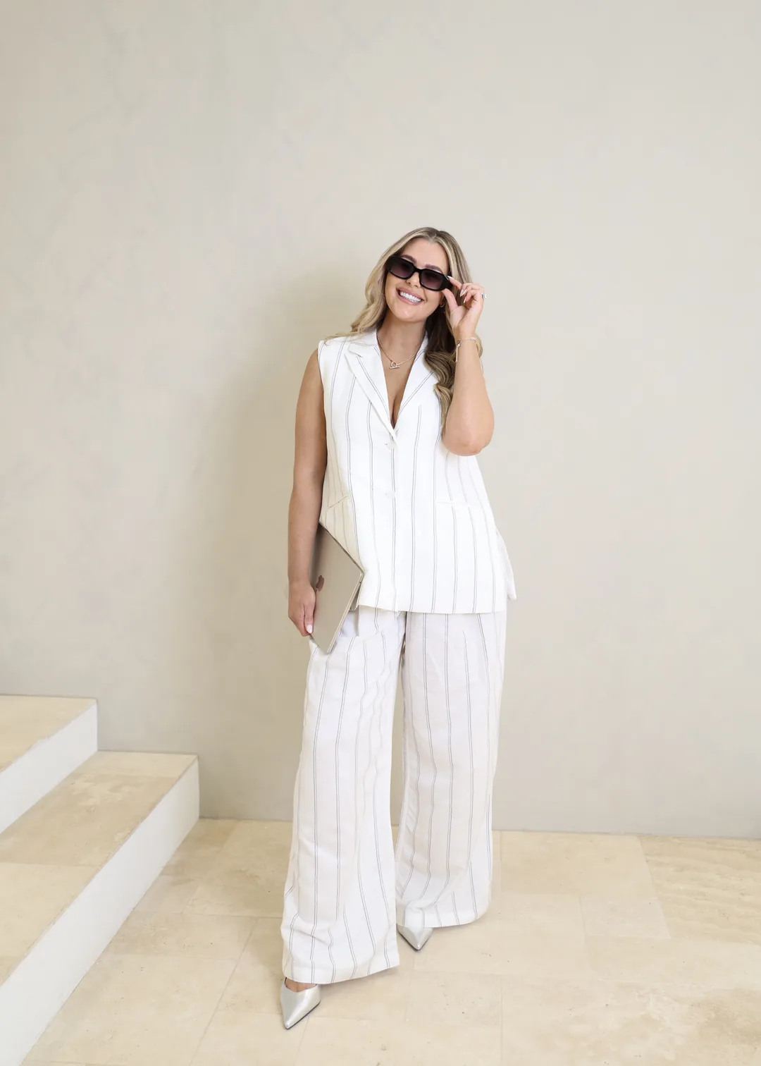 Krystle standing by cream steps in a white pinstripe suit